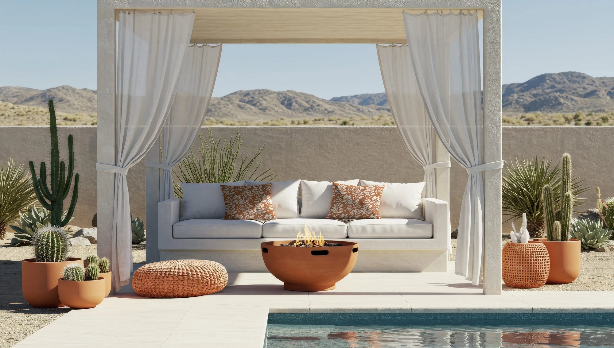 Modern desert patio with white canopy sofa, patterned orange Buffalo Bunny pillows, fire pit, potted cacti, and pool overlooking mountains.