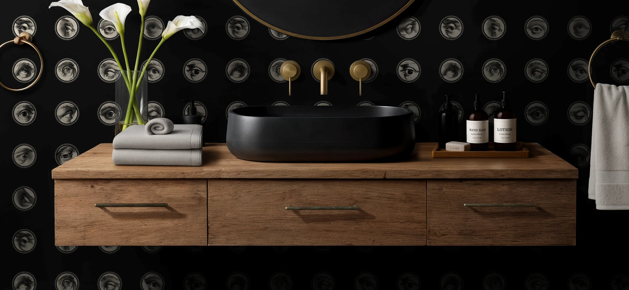 Bathroom vanity with black sink, gold fixtures, and decorative elements against a black wallpaper with circular patterns from Buffalo Bunny.