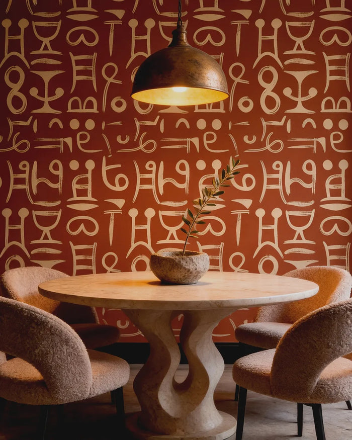 Dining area with a round table and chairs against a wall featuring the Ancient Script Wallpaper.