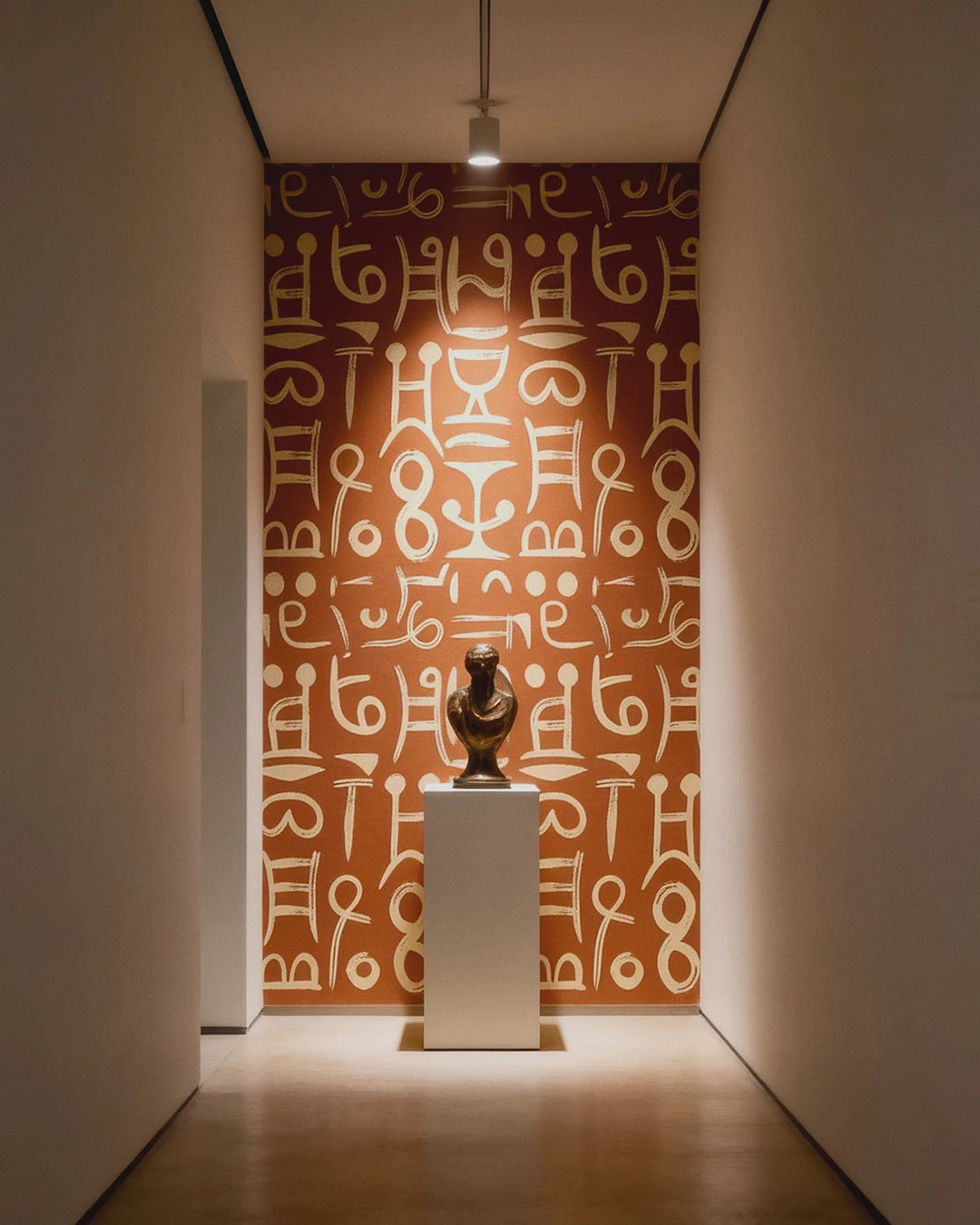 Gallery hallway showcasing a sculpture on a pedestal in a museum setting and a wall featuring the Ancient Script Wallpaper.