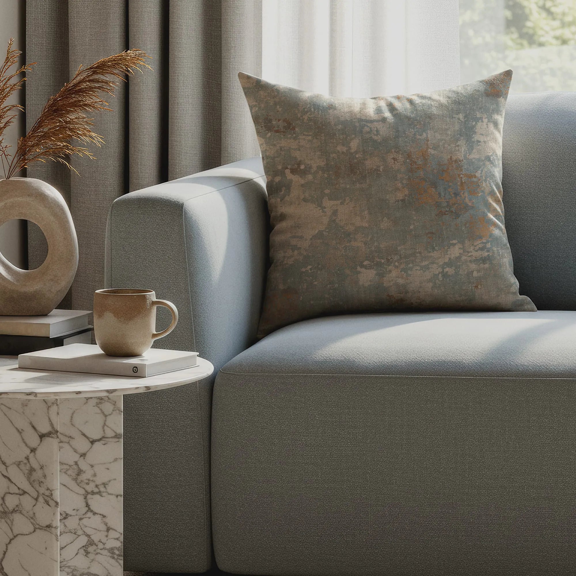 Throw pillow with subtle abstract pattern in muted blue and beige tones on modern light gray sofa beside marble side table.