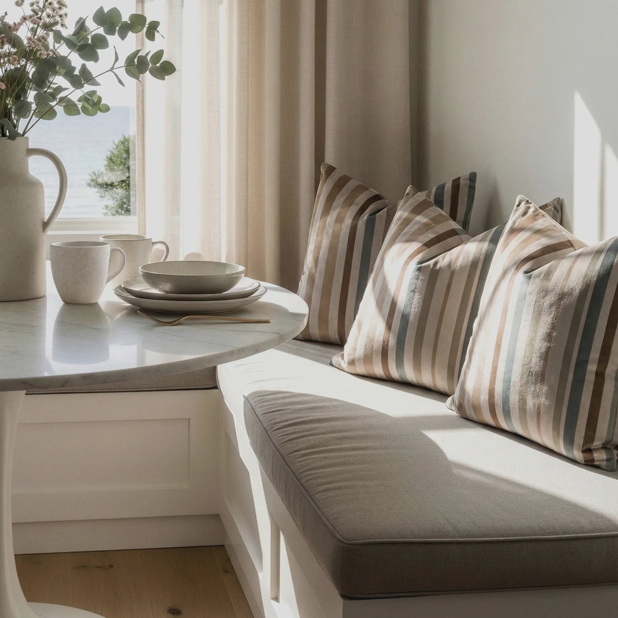 Nook with cushions, a small table with a cup and saucer, and a plant near a window. By Buffalo Bunny.