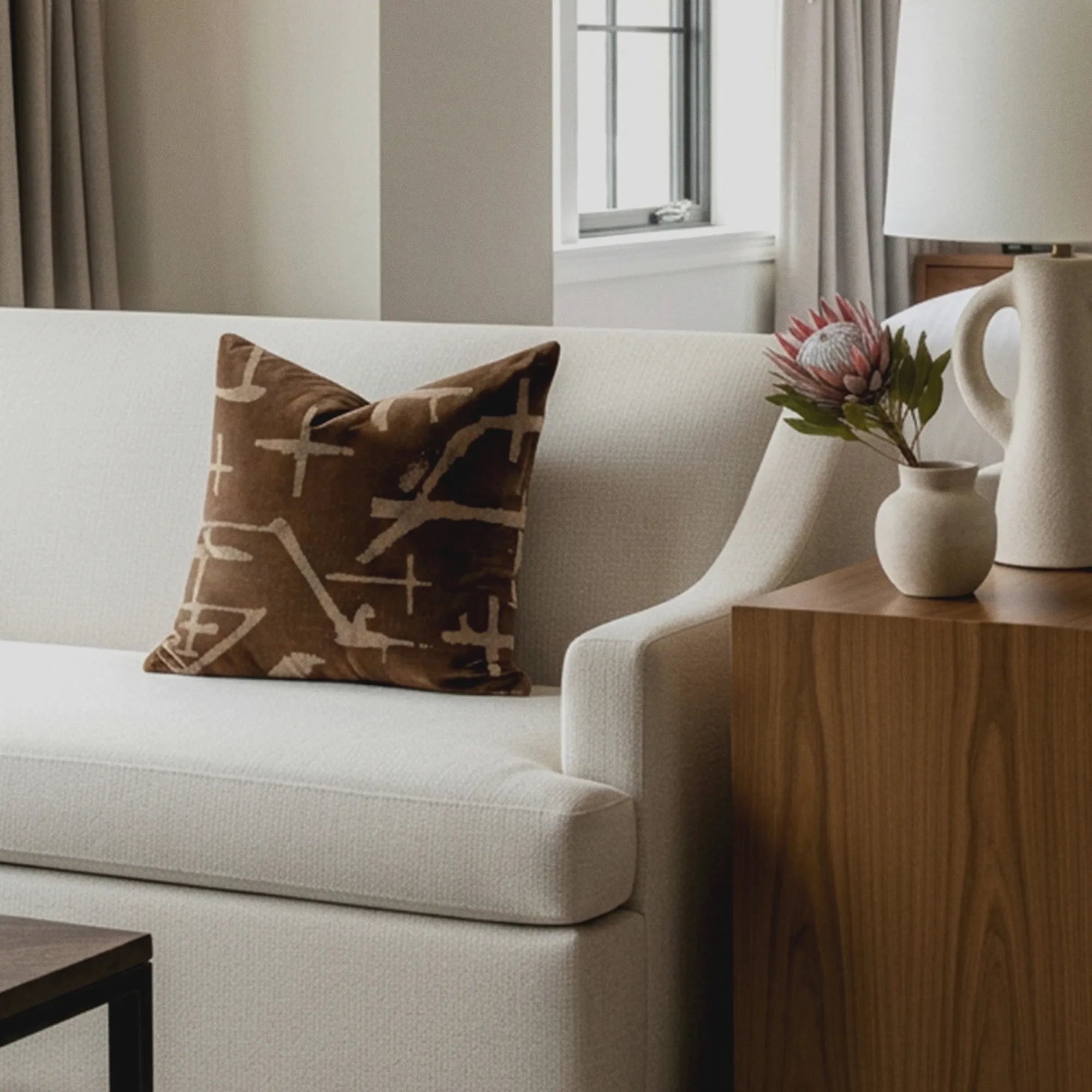 Desert Mark brown abstract-mark pillow on a white boucle sofa beside a wood side table and protea bloom