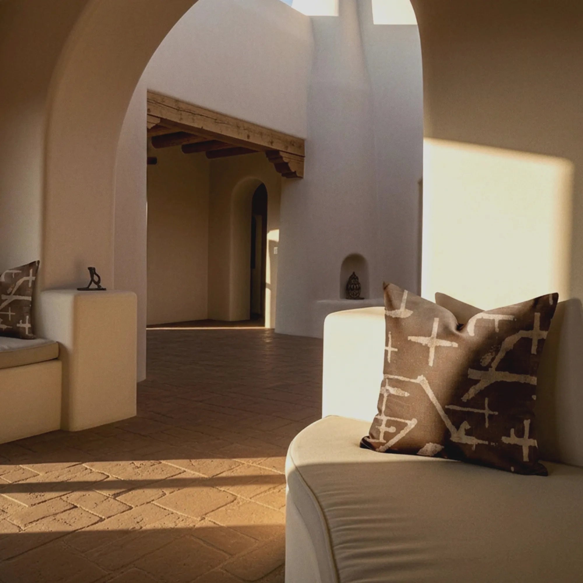 Desert Mark pillows in golden afternoon light on a cream seat inside a white stucco arched interior