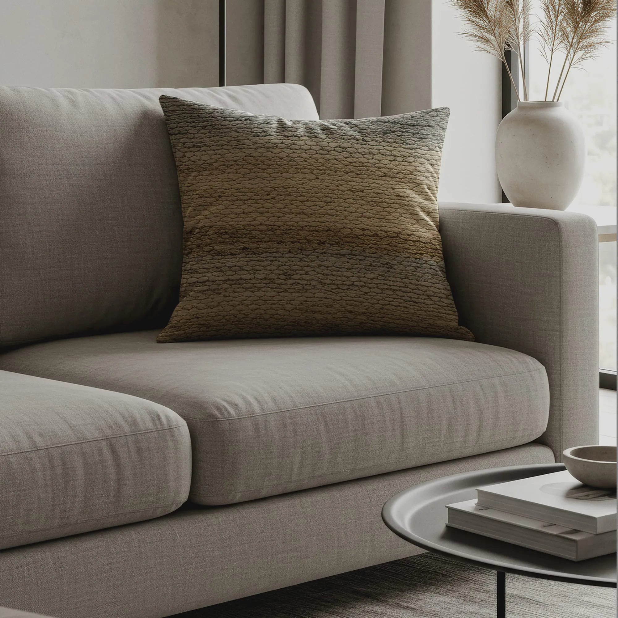 Textured throw pillow with gradient pattern in muted beige, olive, and brown tones on modern light gray sofa.