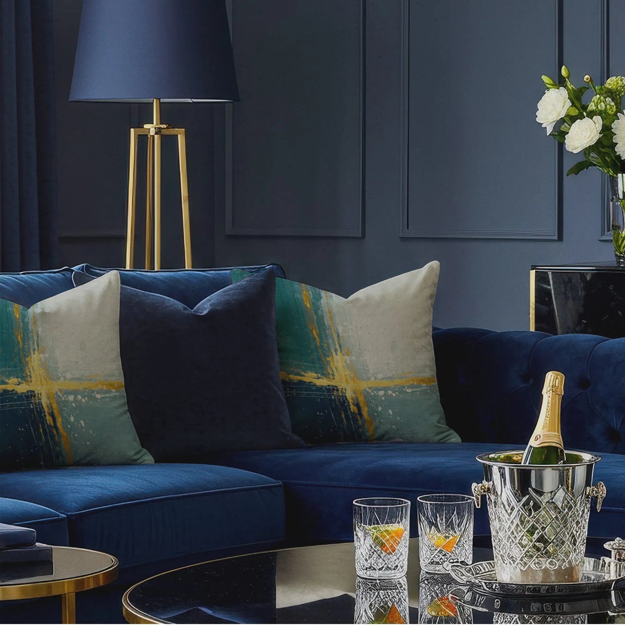 Abstract throw pillows with teal, cream, and yellow brushstroke design on deep blue velvet sectional in elegant living room.