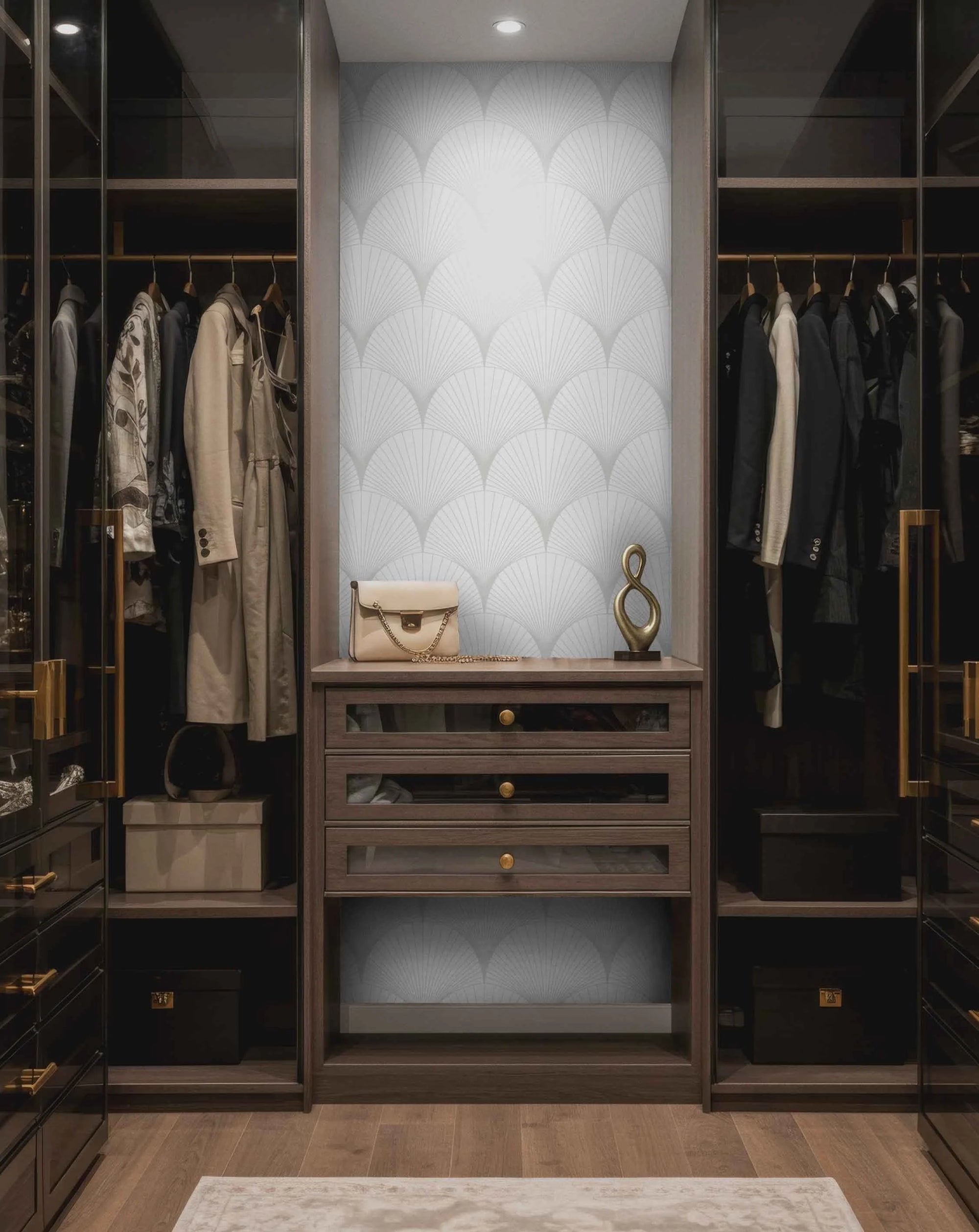 A modern walk-in closet with wooden shelves, clothing, and decorative accents, featuring a geometric light gray fan-patterned wallpaper on the center wall.