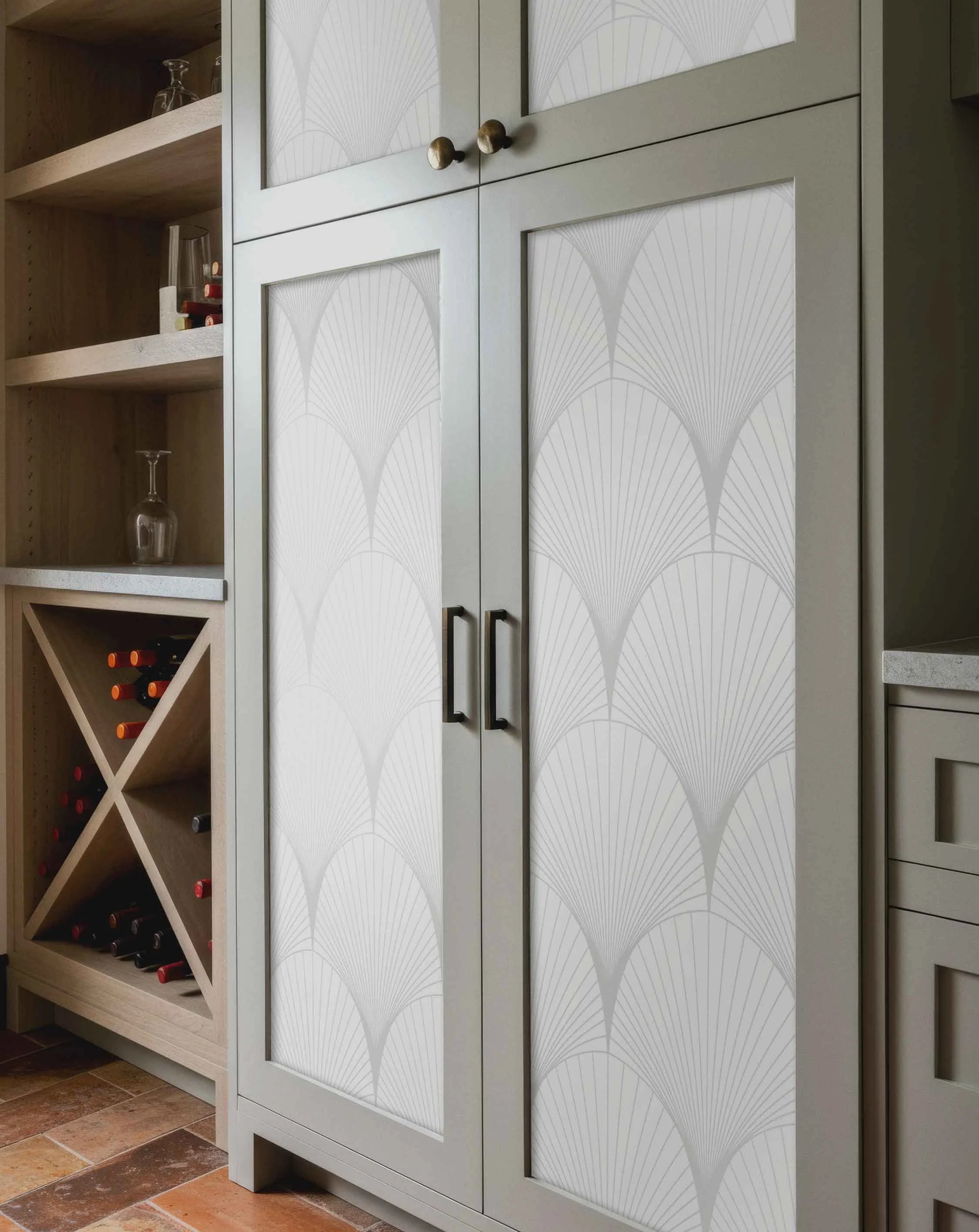 Light gray wine cabinet with wine bottles and glasses. The door of the cabinet is decorated with a geometric light gray fan pattern wallpaper.