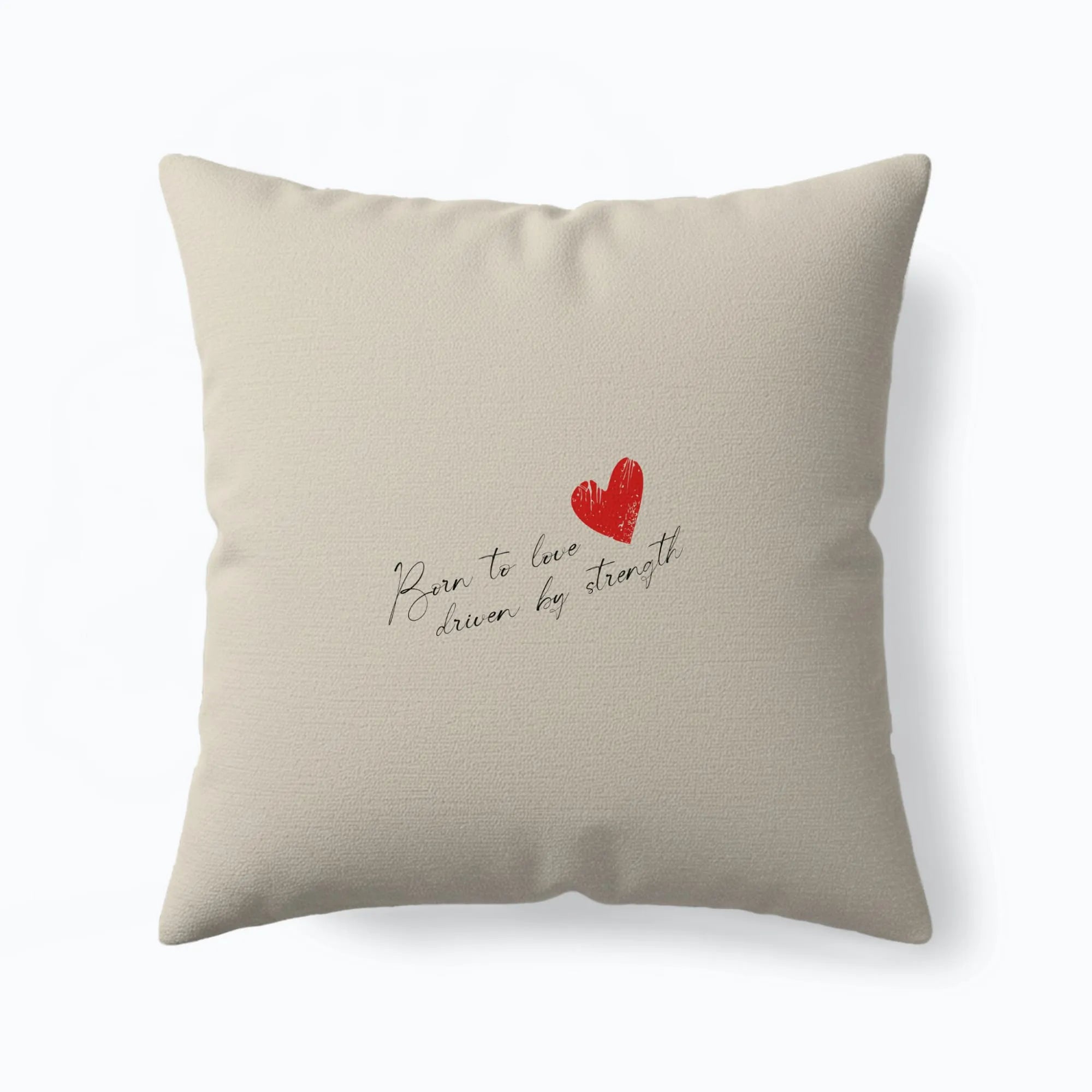 Beige throw pillow with handwritten script “Born to love driven by strength” and small red heart accent.