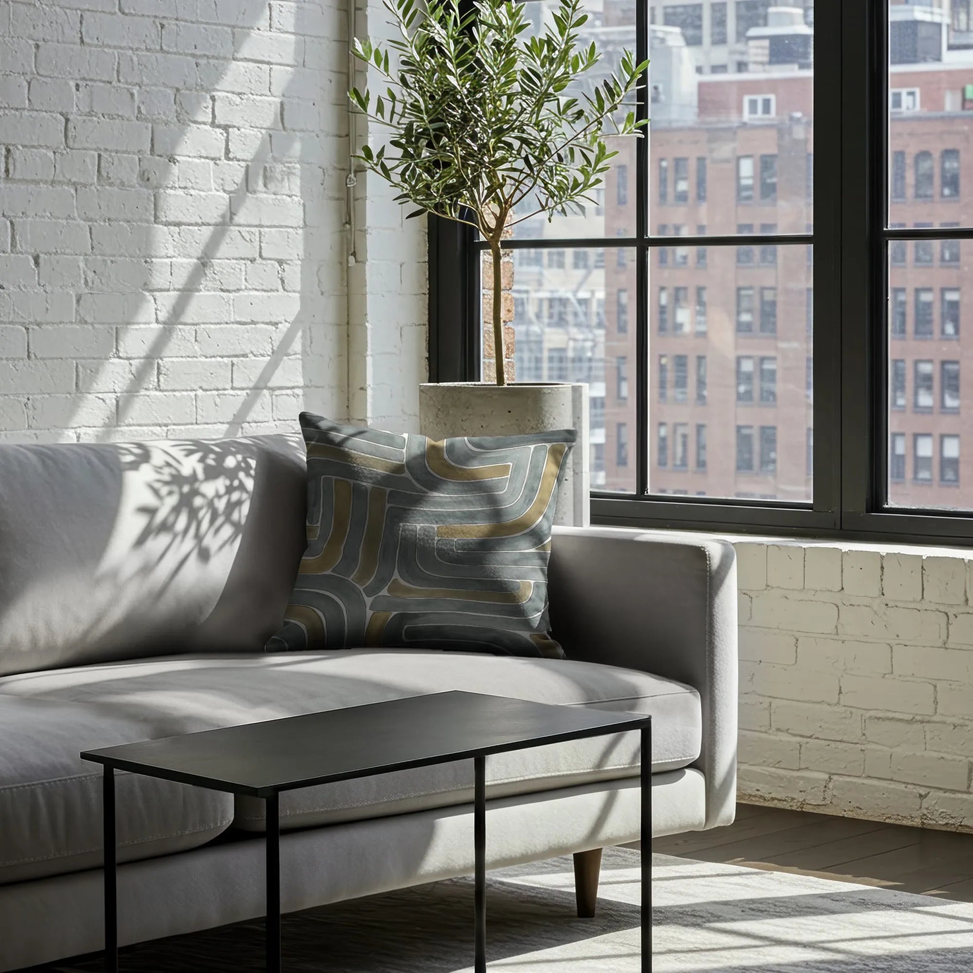 Geometric abstract Buffalo Bunny pillow in grey, olive, and cream tones on grey velvet sofa in Soho loft with concrete planter