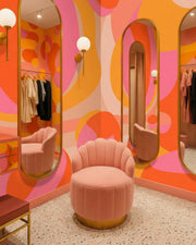 Pink chair in a room with colorful, abstract wall patterns and mirrors. By Buffalo Bunny.