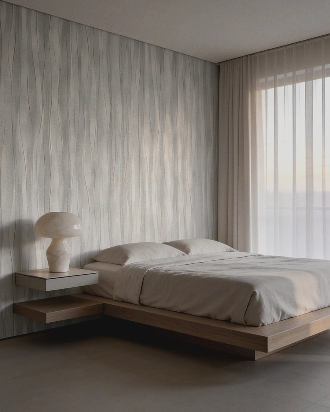 A minimalist modern bedroom featuring a low floating platform bed with beige bedding, a matching mushroom-shaped table lamp on a floating side table, and a large wall panel with they grey Soft Current Wallpaper.