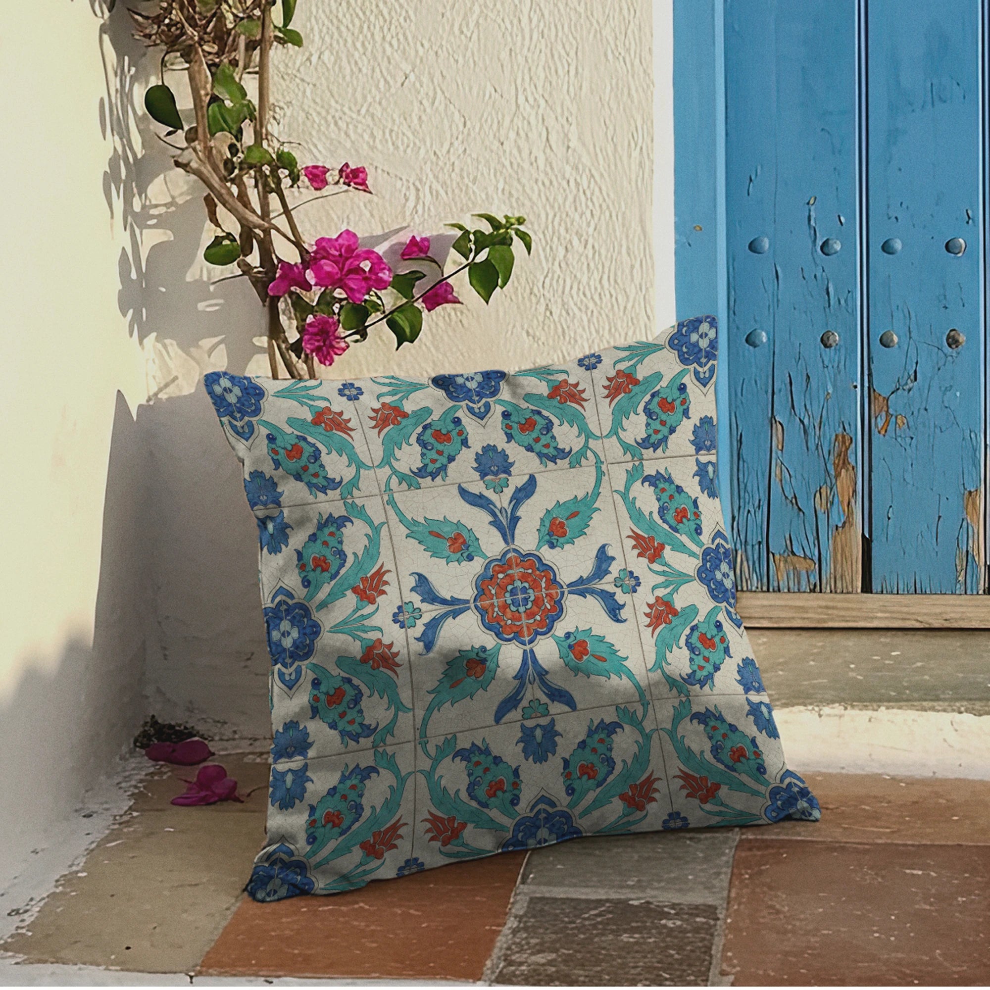 Mediterranean-style entrance featuring a boho tile-print pillow with teal, blue, and rust colors, vibrant bougainvillea flowers, and a weathered blue wooden door.