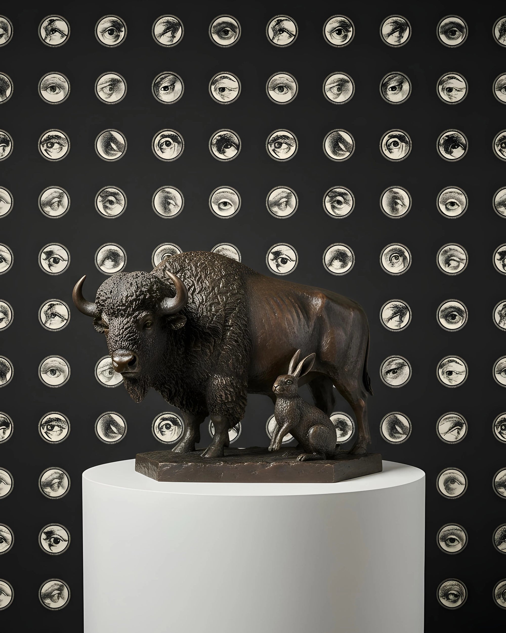 Bronze sculpture of a bison on a white pedestal against a black background with circular eye patterns from Buffalo Bunny.