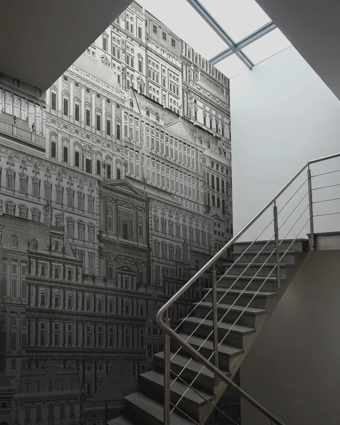 Palazzo Grande wallpaper mural rising up a stairwell wall beside a metal staircase under a skylight